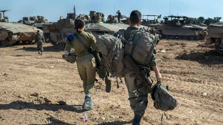 Kaksi israelilaissotilasta kävelemässä kuvattuna takaapäin, taustalla panssarivaunuja.
