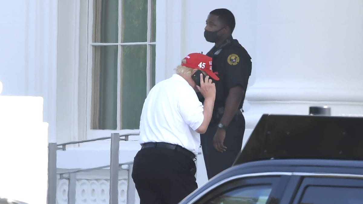 Trump puhuu kännykkään. Taustalla seisoo poliisi.