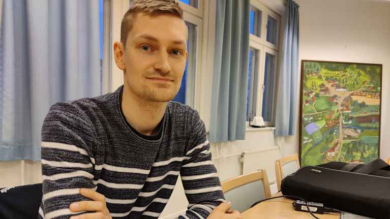 En man sitter vid ett bord med armarna i kors. Han heter Emil Hästbacka.