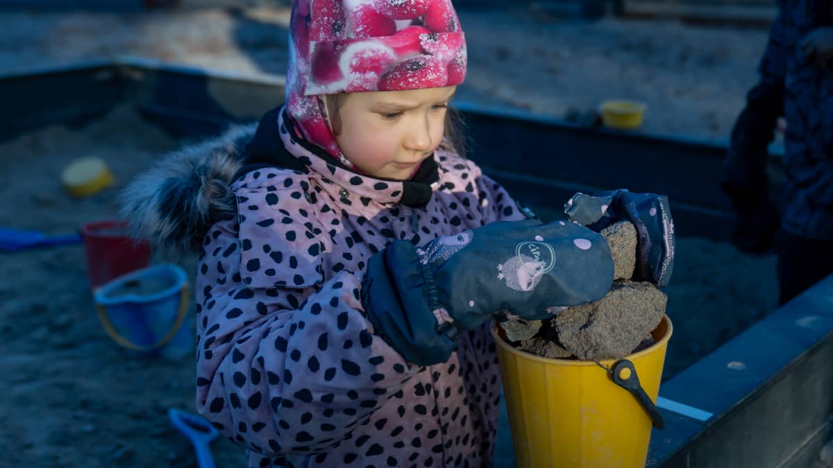 Helsinkiläisen päiväkoti Tunturin "metsätonttu" ryhmän (4-5 vuotiaat) päiväkotilapsi Mia leikkimässä hiekkalaatikolla, Vesala, 16.11.2023.