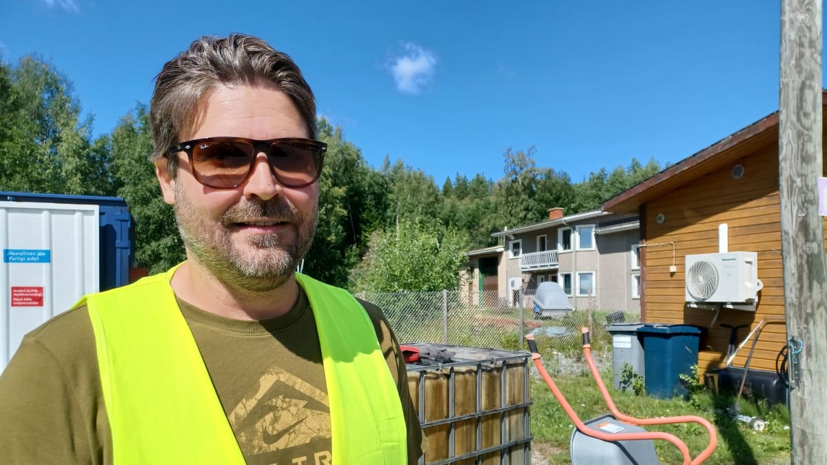 En ung man i solglasögon och en gul arbetsväst står på en återvinningscentral