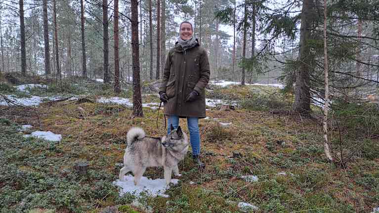 Daniela Andersson står en skog med lite snö på marken. Hon har sin hund Orvar i koppel.