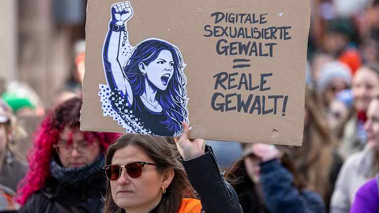 En kvinnlig demonstrant håller upp en tyskspråkig skylt med texten: "Digitalt sexualiserat våld = verkligt våld".