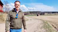 Tomas Gripenberg står vid en åker där det kör en traktor långt i bakgrunden.