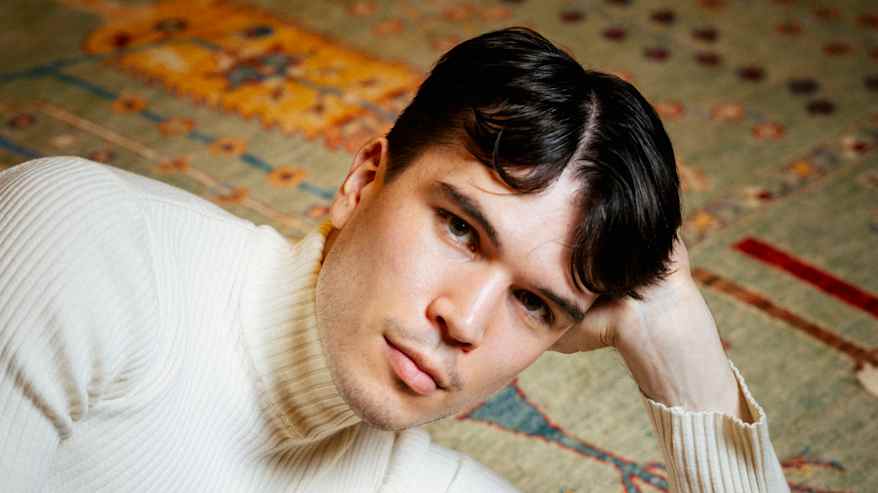 A person dressed in a light sweater is lying on a green carpet.