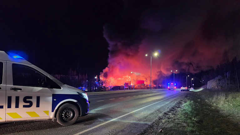 A police van blocks a motorway, with a large fire and smoke seen in the distance.