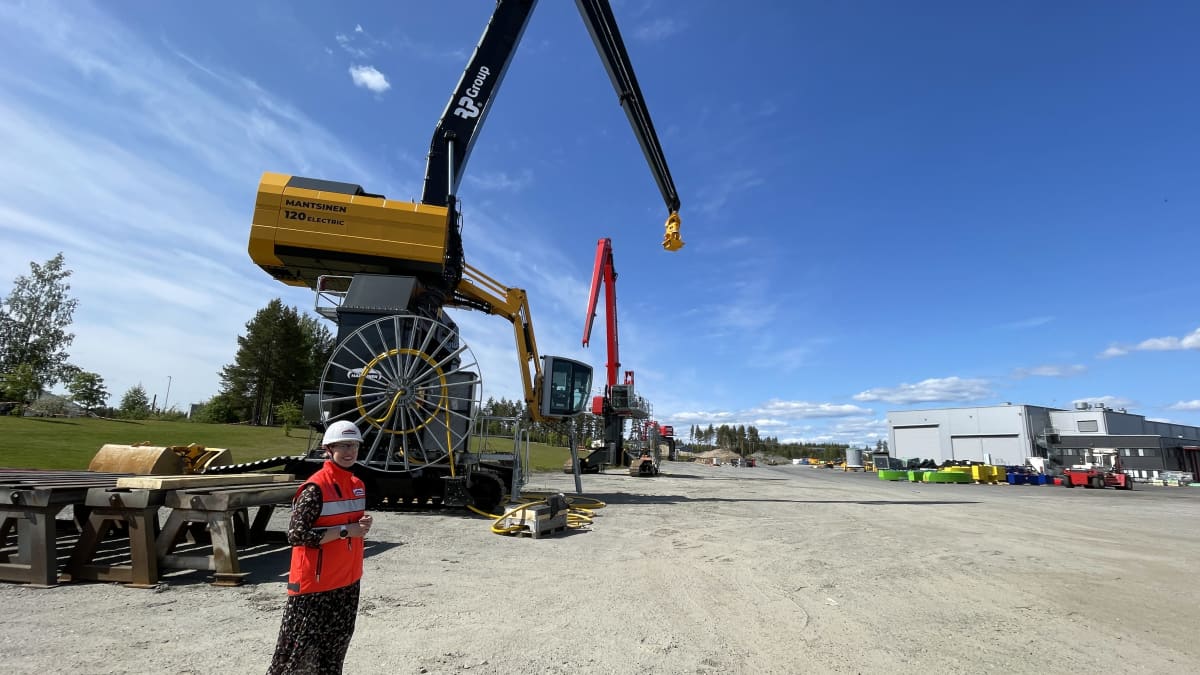 Mantsinen Groupin toimitusjohtaja Mia Mantsinen yrityksen ulkopihalla isojen materiaalinkäsittelynostureiden edessä valkoinen suojakypärä päässään.