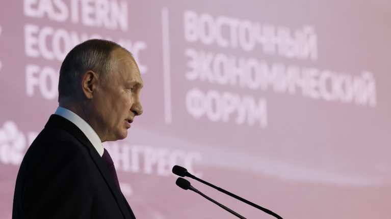Vladimir Putin puhuu kahteen mikrofoniin. Hänellä on musta puku ja valkoinen kauluspaita. Taustakankaassa lukee Eastern Economic Forum, siis Itäinen talousfoorumi.