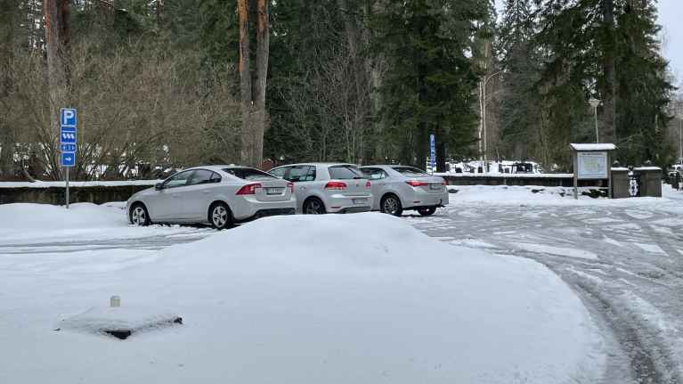 Talvinen maisema Kuopion ison hautausmaan parkkipaikalla ja etualalla kadonneen patsaan jalusta lumen peitossa. 