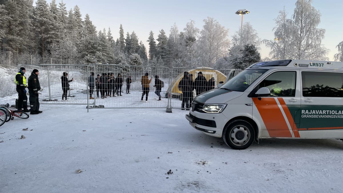 Rajavartiolaitoksen auto ja takana aitaus jonka sisällä teltta ja ihmisiä. 