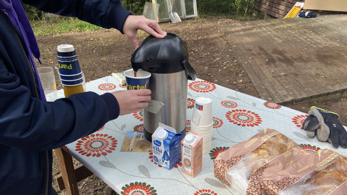 En persons händer syns som tar kaffe i en kaffetermos utomhus.