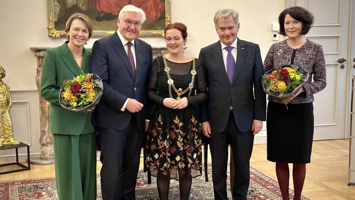 W rzędzie stoją trzy formalnie ubrane kobiety i dwóch starszych mężczyzn ubranych na szaro.