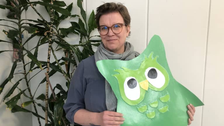 Heli Sandström katsoo kameraan ja pitää käsissään isoa vihreää paperipöllöä.