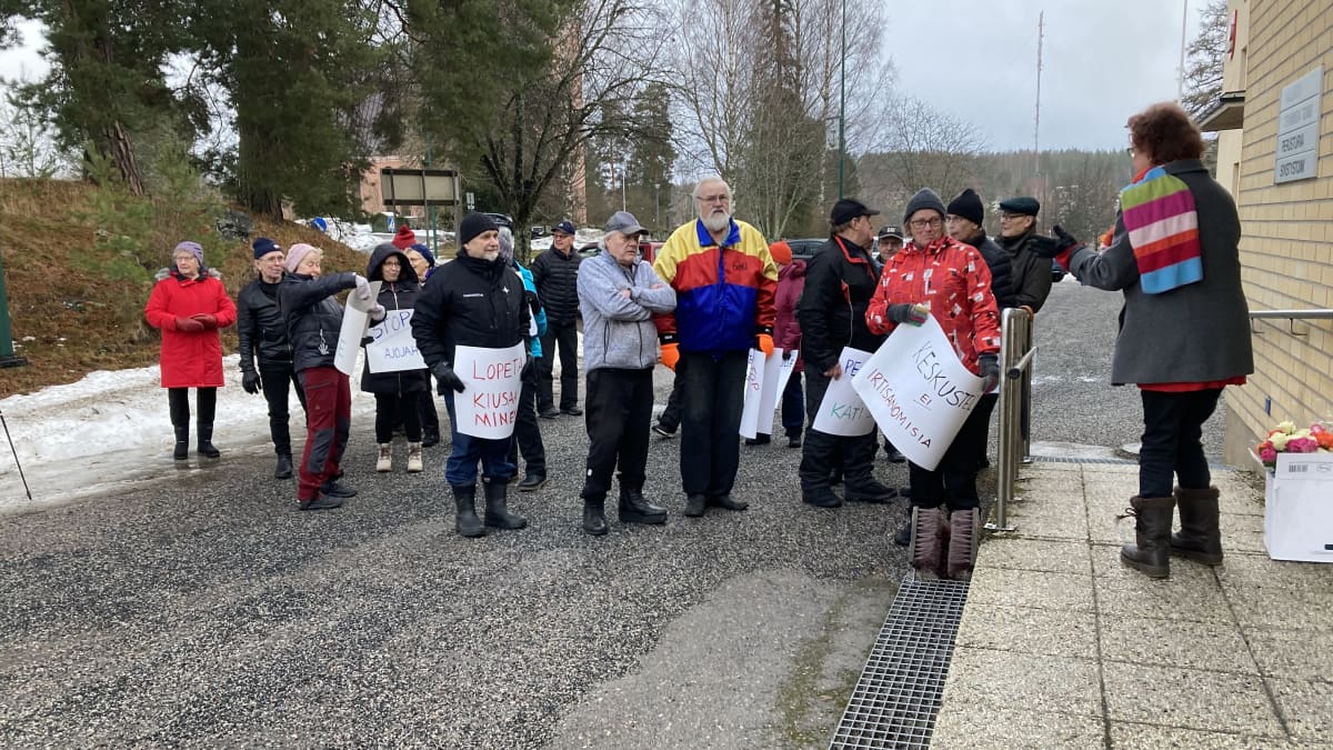 Joukko ihmisiä. Osalla heistä käsissään on papereita, joihin on kirjoitettu iskulauseita kuten "lopeta kiusaaminen" ja "keskustelua, ei irtisanomisia".