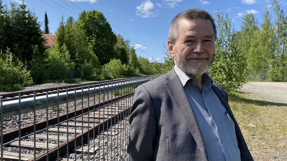 Suomen Lähijuna Oy:n johtohahmo Antero Alku katsoo kameraan junaradan varrella ja hymyilee.