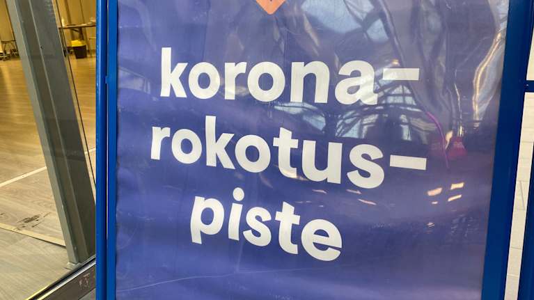 Koronarokotuspiste -teksti muovilla suojatussa sinisessä julisteessa.