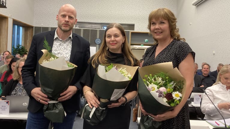 Aleksi Jäntti, Johanna Loukaskorpi ja Erja Pelkonen seisovat kukkakimput sylissään Pirkanmaan aluevaltuustossa.