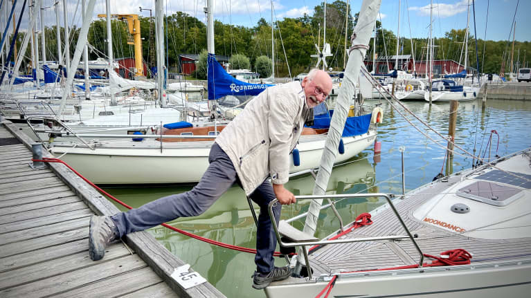 Leif Kronberg kurottautuu purjeveneeseensä, toinen jalka laiturilla, toinen veneessä, Turun Pursiseuran rannassa.