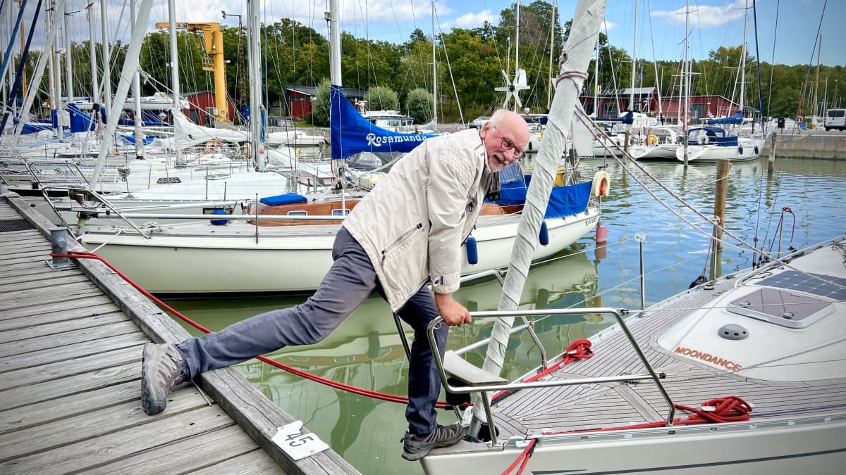 Leif Kronberg kurottautuu purjeveneeseensä, toinen jalka laiturilla, toinen veneessä, Turun Pursiseuran rannassa.