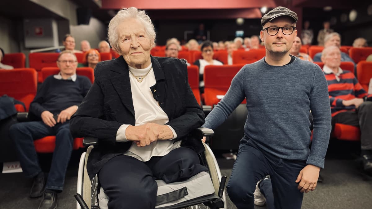 Siiri Rantanen ja dokumenttiohjaaja Jani Wallenius poseeraavat kameralle elokuvateatterissa. Taustalla näkyy yleisöä.