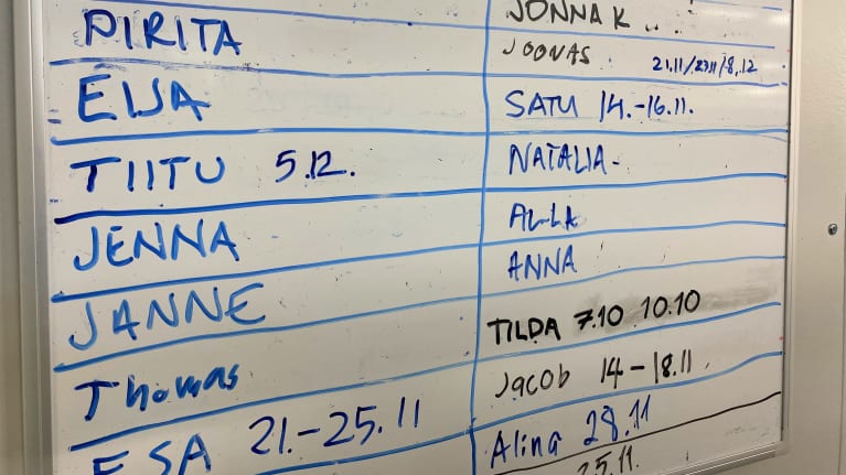 Lähikuva seinätaulusta, johon kirjoitettu työntekijöiden nimet ja päivämääriä. Taulu Bevenic Elektropointin tiloissa Hollolassa.
