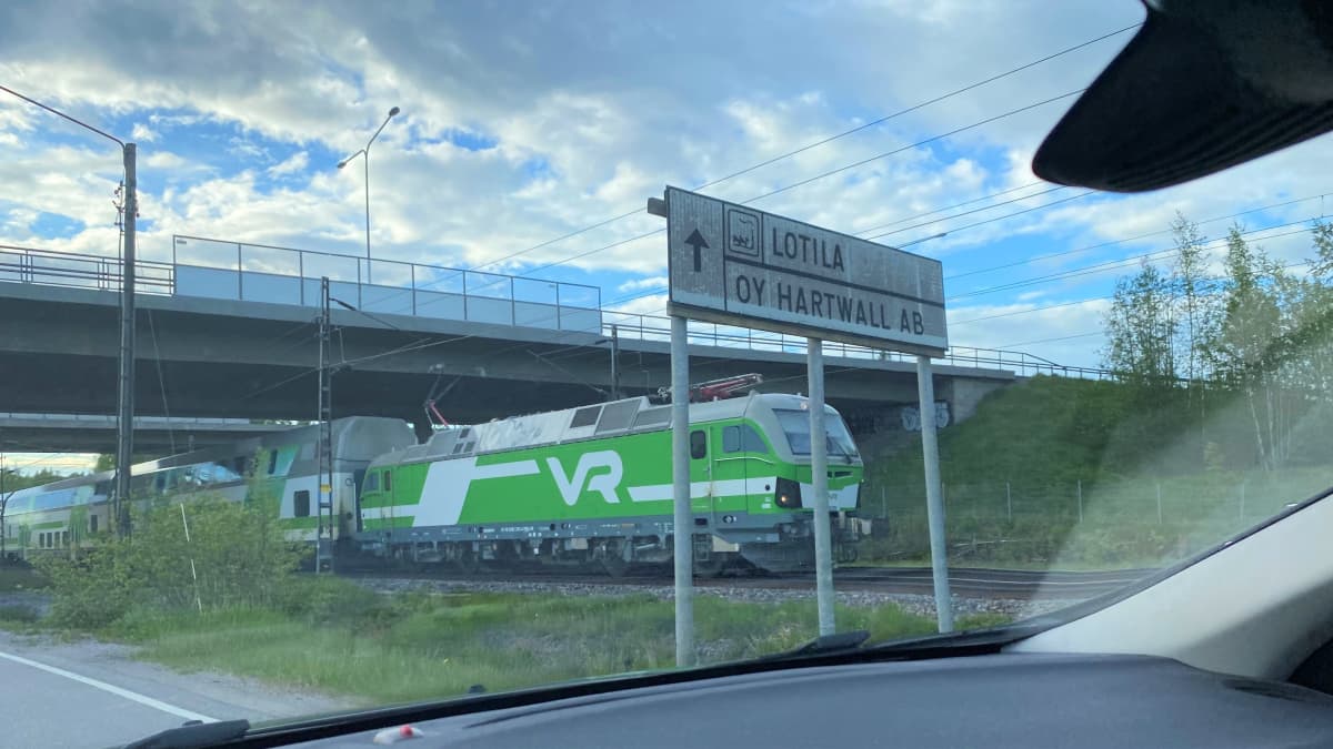 Juna raiteillaan sillan ali, kuva otettu autosta joka ajaa tiellä junan ohi. Kuva otettu Lahdessa