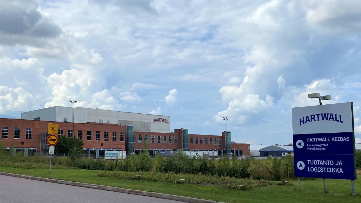 punatiilinen iso tehdasrakennus aitauksen takana, rekka-autoja pihassa