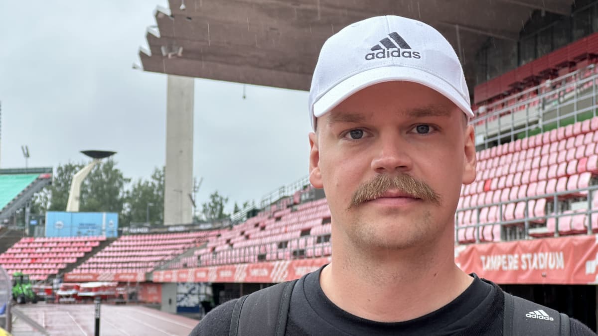 Mies katsoo kameraan tyhjän stadionkatsomon edessä.