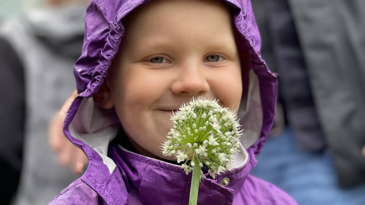 En närbild på ett barn som håller en blomma framför ansiktet.
