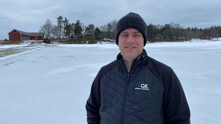 Jorbrukare i svart mössa och gråblå overall på snöig och isig åker i Kimitoöns kommun.