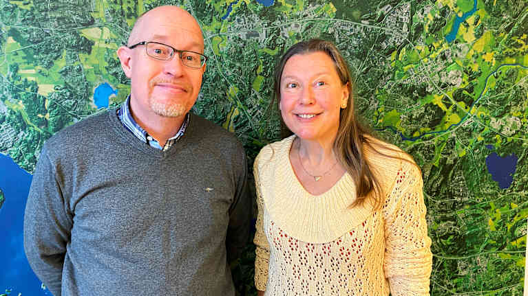 Äldre manlig och kvinnlig forskare ler in i kameran framför en karta av Åbo skärgård. 