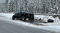 Photo shows a crashed car on the side of a snowy road.