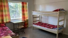 Kerrossänkyjä huoneessa, ikkunaa vasten pieni pöytä ja tuoli.