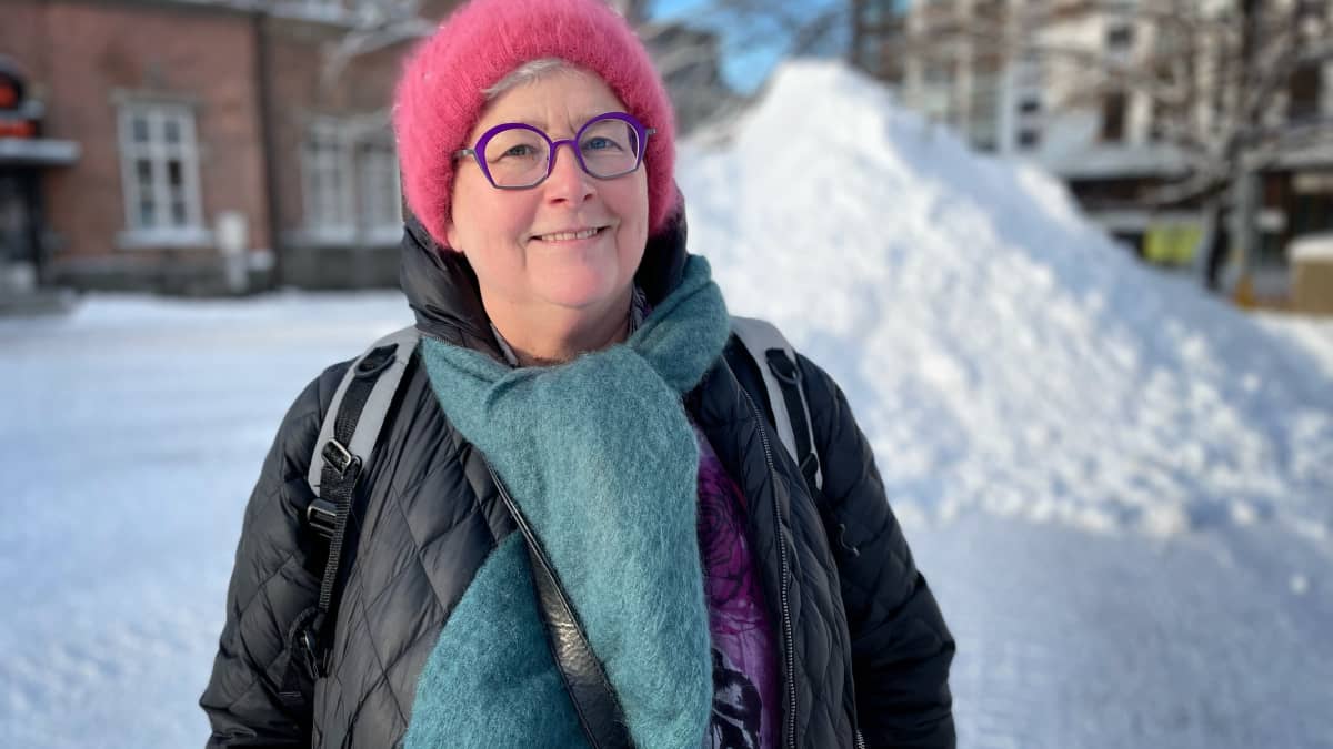 Hymyilevä Vuokralaiset ry toiminnanjohtaja Anne Viita punaisessa angorapipossa Tullintorin aukiolla Tampereella. Taustalla punatiilinen rakennus ja iso lumikasa. 