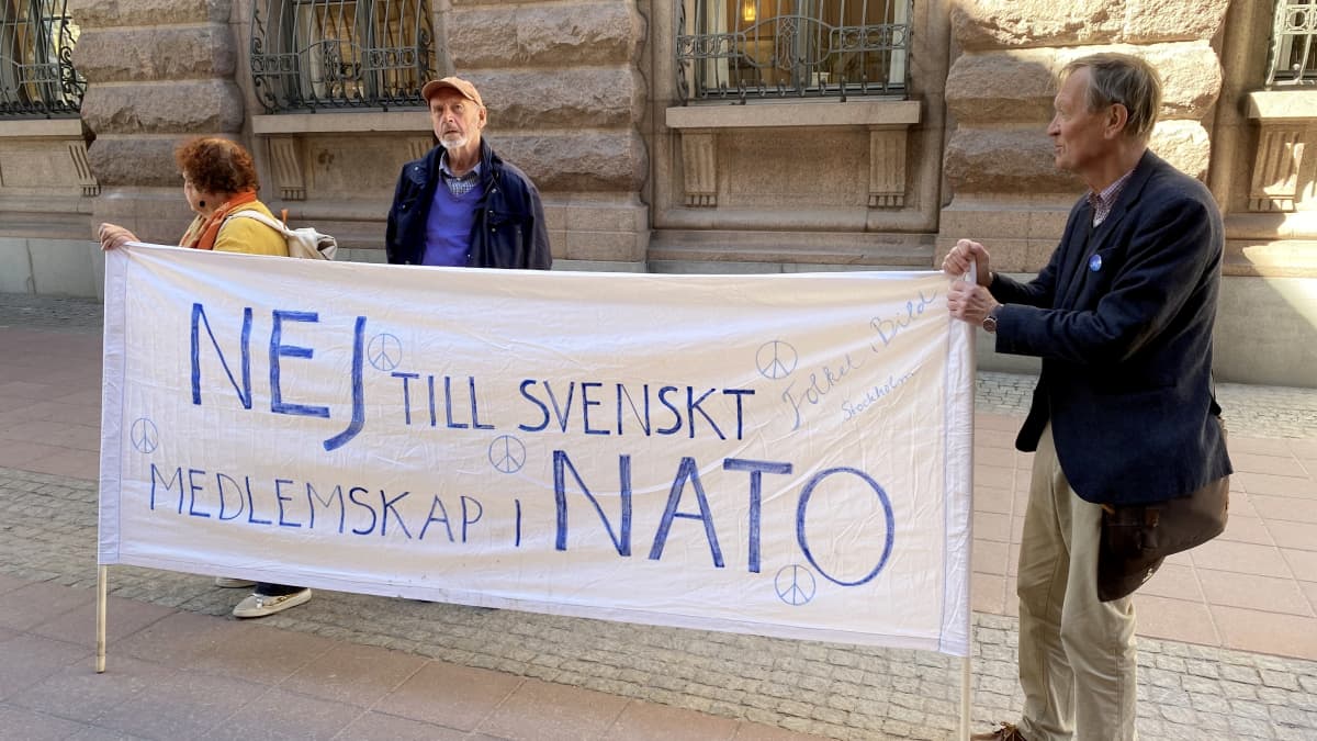 Mielenosoittajia Natoa vastustavan lakanan kanssa.