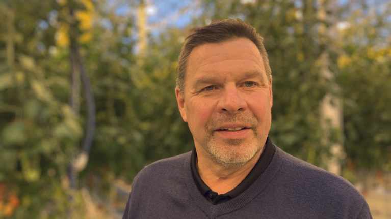 Mansperson i växthusmiljö. I bakgrunden syns tomatplantor.