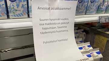 kaupan maitohylly, jossa on lappu. Siinä lukee, että suuren kysynnän vuoksi osa tuotteista on päässyt loppumaan. 
