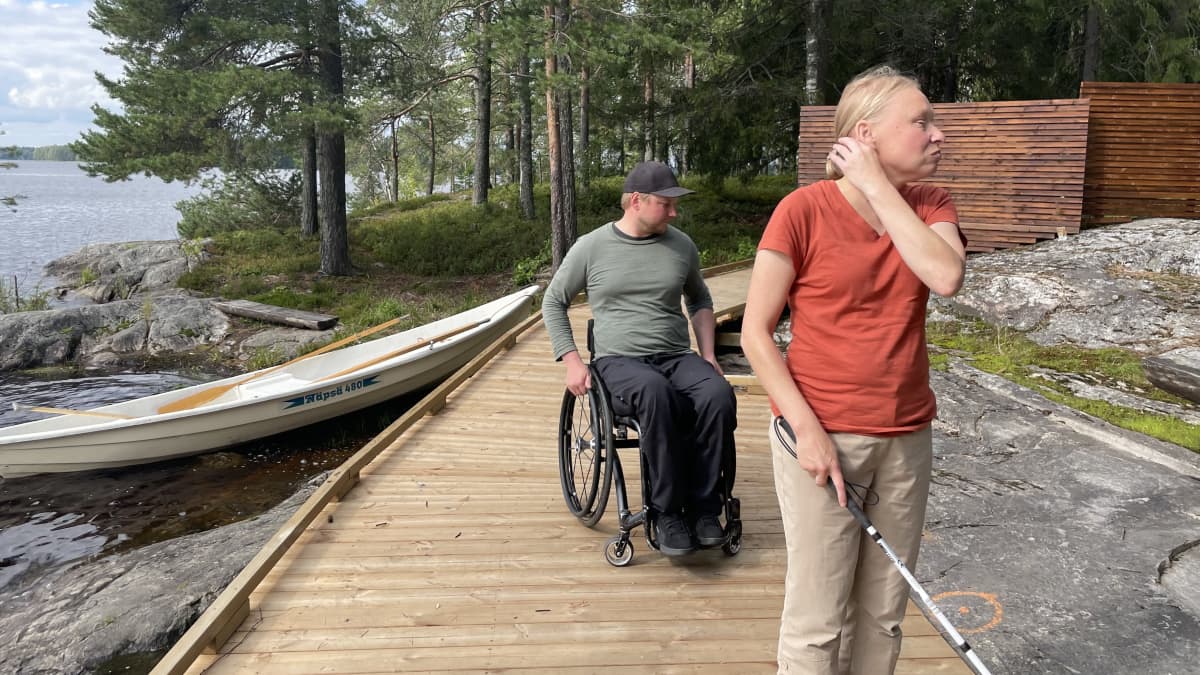 Nainen sokeainkepin etualalla mies pyörätuolissa testaamassa esteetöntä saarta.