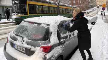 Nainen puhdistaa lumia autonsa päältä.