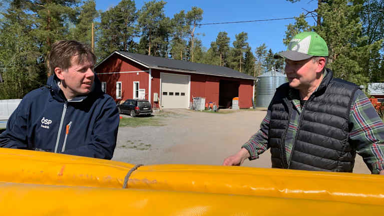 Två män stor vid en gul pressenning på en gårdsplan till ett lantbruk