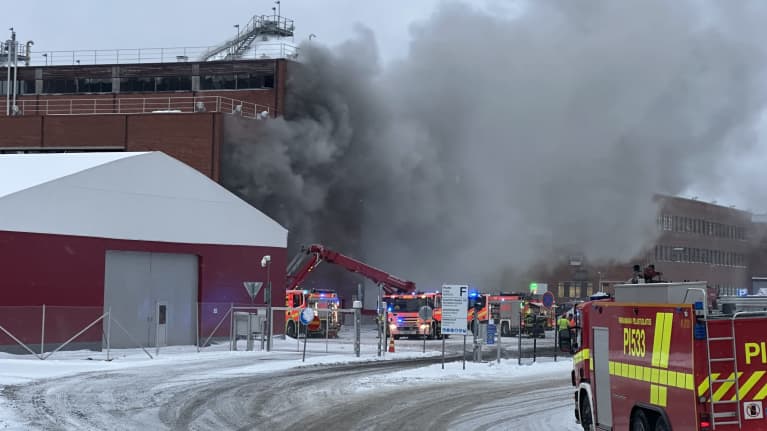 Tulipalo Nokian paperitehtaalla. Kuvassa punatiilisestä rakennuksesta nousee paksua mustaa savua, pelastushenkilökuntaa korkean nosturin päällä. Kuvauspäivä 29.11.2023.