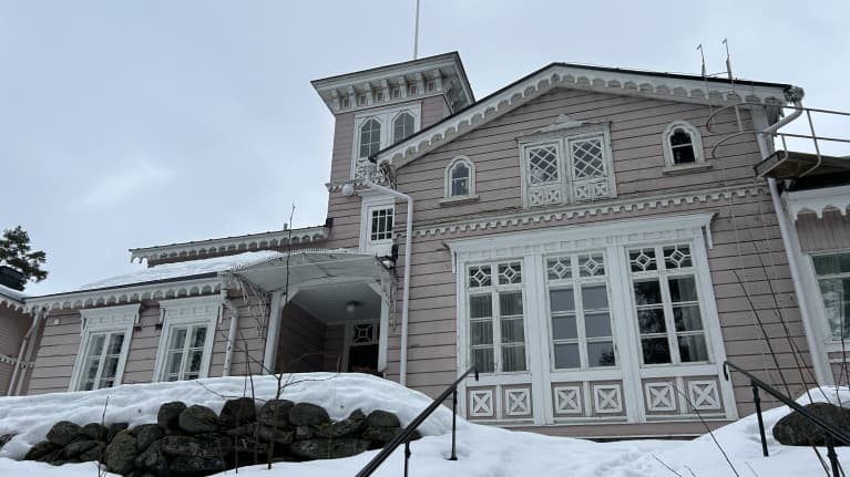 Puurakenteisen vaaleanpunaisen Hotelli Punkaharjun koristeellinen julkisivu kuvattuna mäen päällä lumen keskellä.