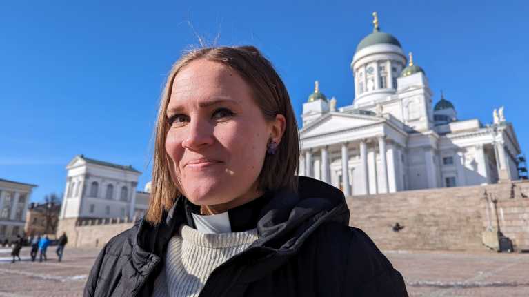 Marjut "Maikki" Mulari seisoo Helsingin tuomikirkon edessä aurinkoisena päivänä.