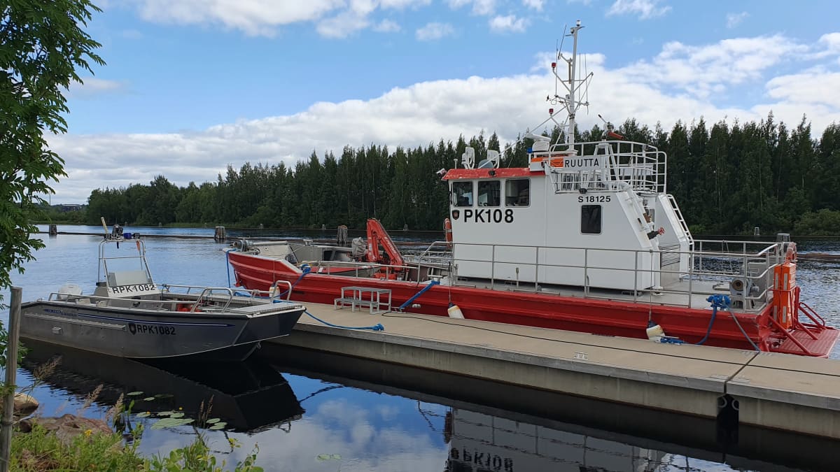 Pohjois-Karjalan pelastuslaitoksen laiva Ruutta ja moottorivene sidottuna venelaituriin Joensuussa Pielisjoella puolipilvisenä kesäpäivänä.
