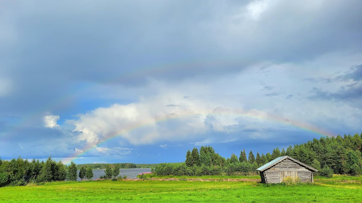 Kesäpäivän maisema Sodankylässä. Peltoa, lato, ukkospilviä ja sateenkaari. 