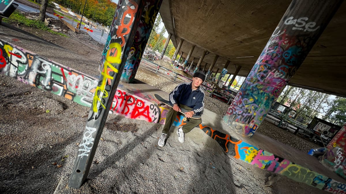 Jon Sallinen istuu rullalauta sylissään laajakuvassa graffiteilla koristellun tiesillan alla.