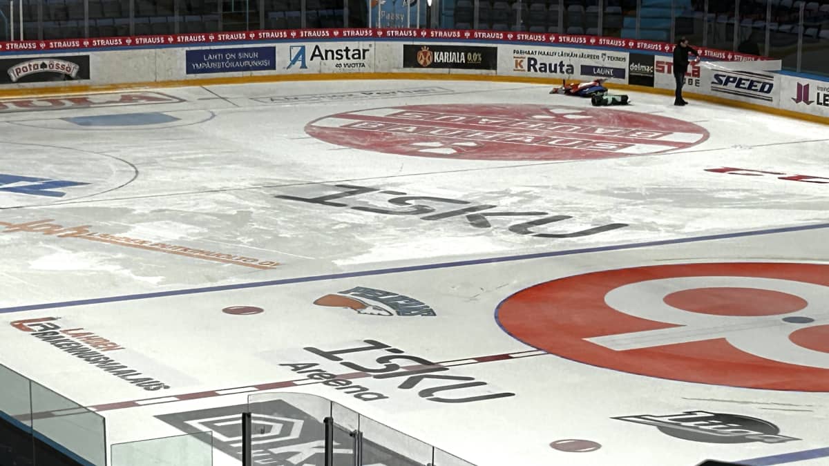 Lähikuvassa on jäähallin jää ja sen mainokset. Ihminen repii kaukalon mainosteippiä pois.