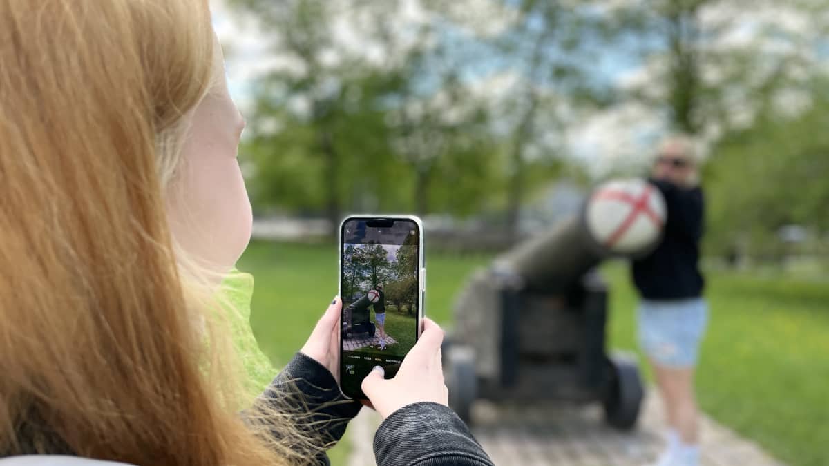 Nuori ottaa kuvaa puhelimella toisesta henkilöstä puistossa.