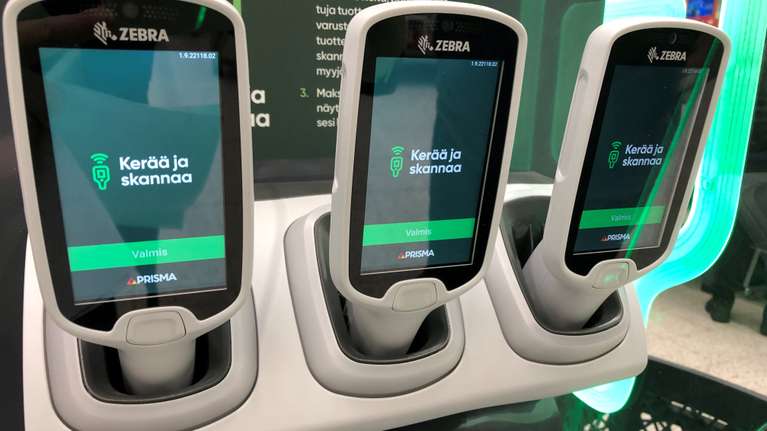 Tre handhållna skannrar i laddstationer med texten "Kerää ja skannaa" och "Prisma" synlig på skärmarnas display.
