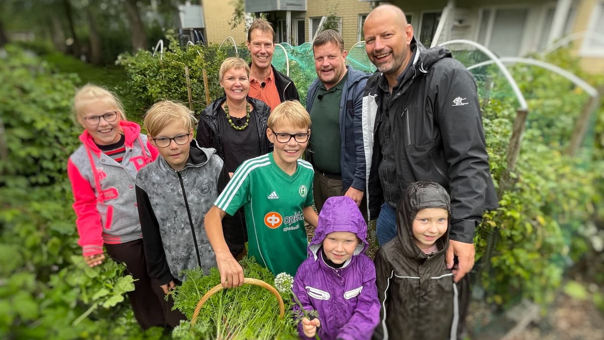 En stor familj står tillsammans ute i en trädgård.